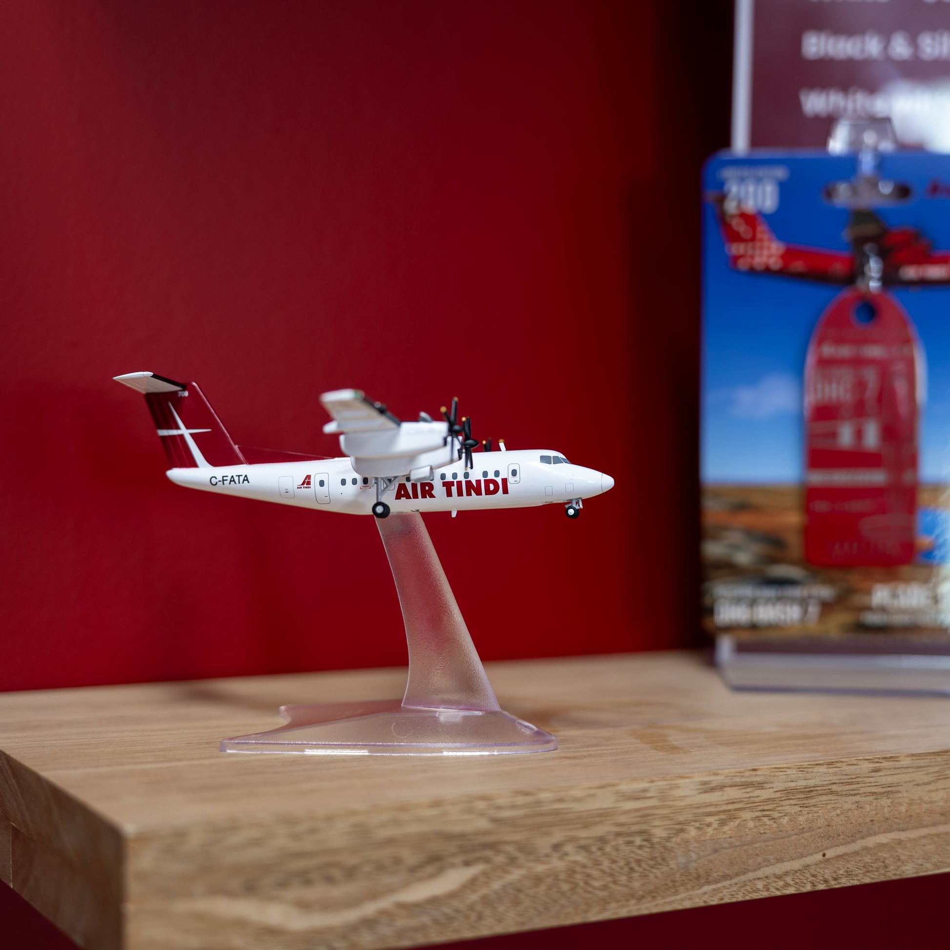 An Air Tindi Dash 7 model displayed on a clear stand on a wooden surface with a red background.