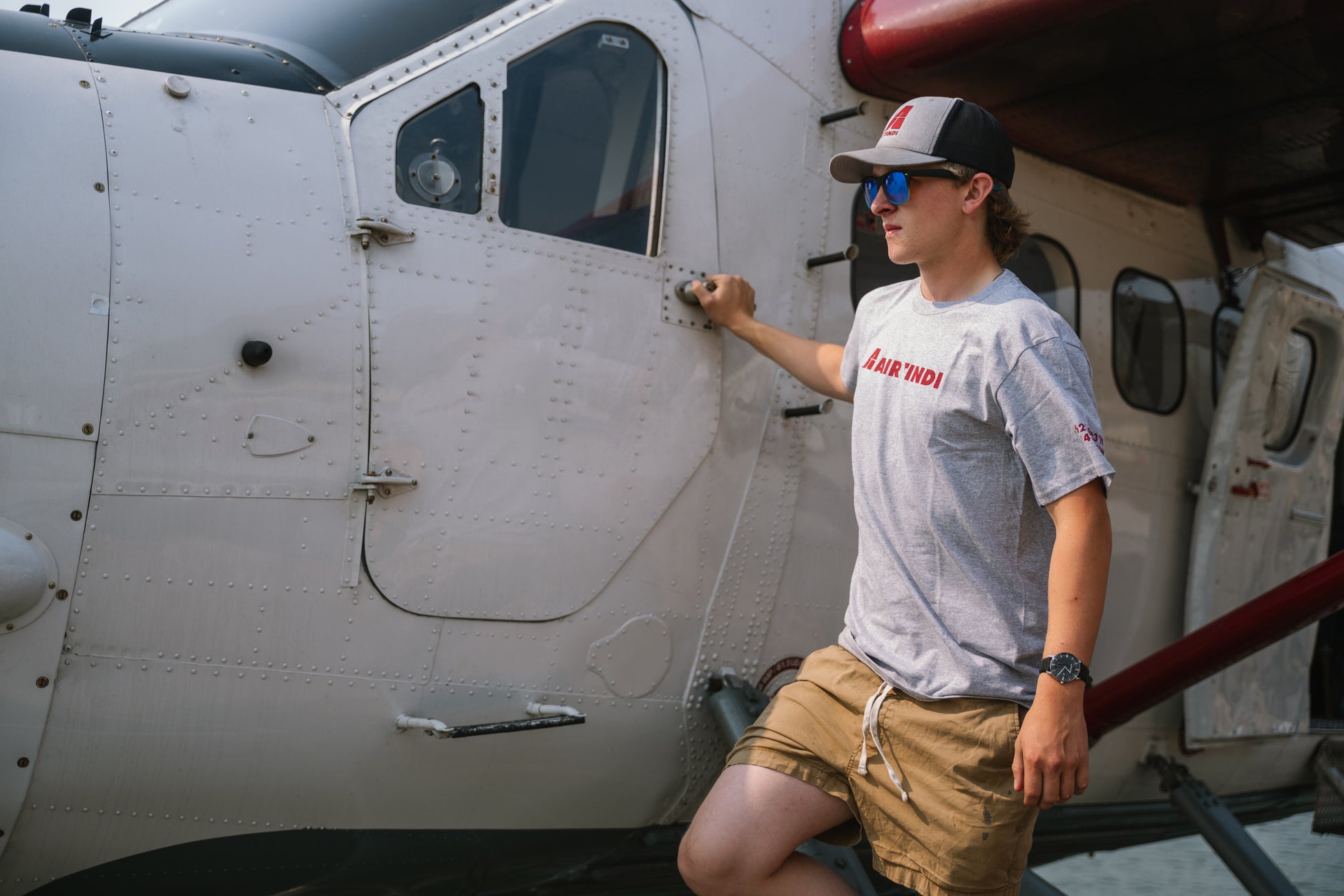 Model wearing an Air Tindi Active Unisex T-Shirt by a floatplane