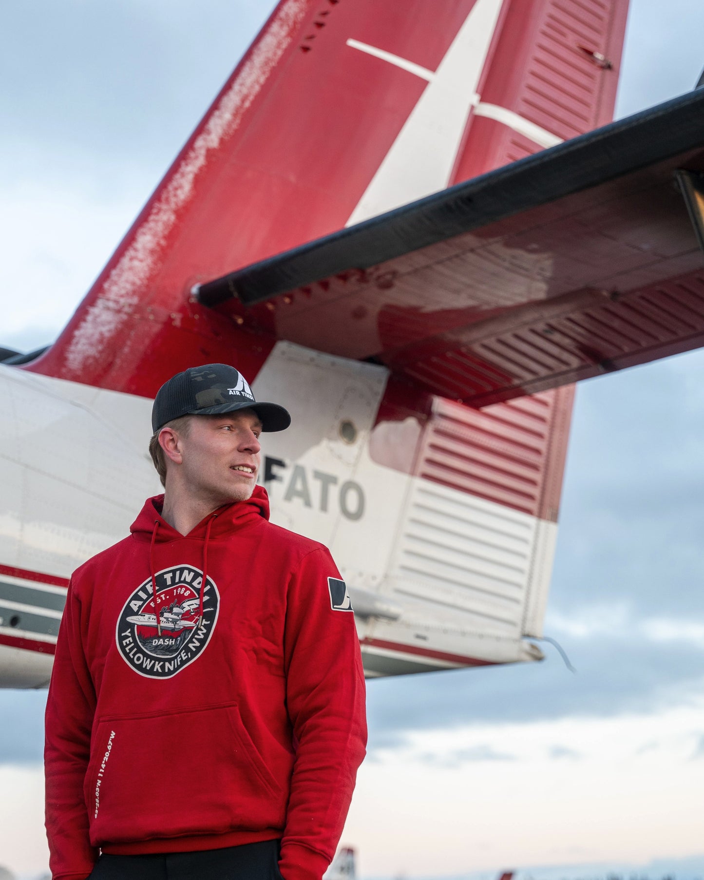 Model wearing an Air Tindi Dash 7 Hoodie with a plane in the background