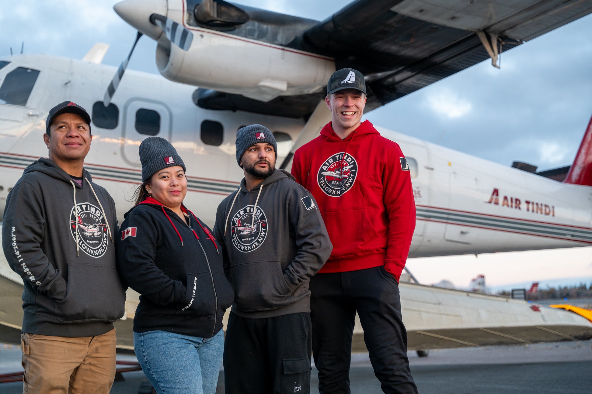 Model wearing an Air Tindi Dash 7 Hoodie, alongside other models wearing a Signature Full Zip Hoodie and Twin Otter Hoodie