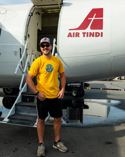 Model wearing the Limited Edition de Havilland Heritage Tee standing in front of an Air Tindi aircraft