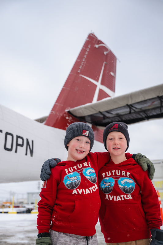 Two models wearing an Air Tindi Future Aviator Youth Hoodie in front of a plane