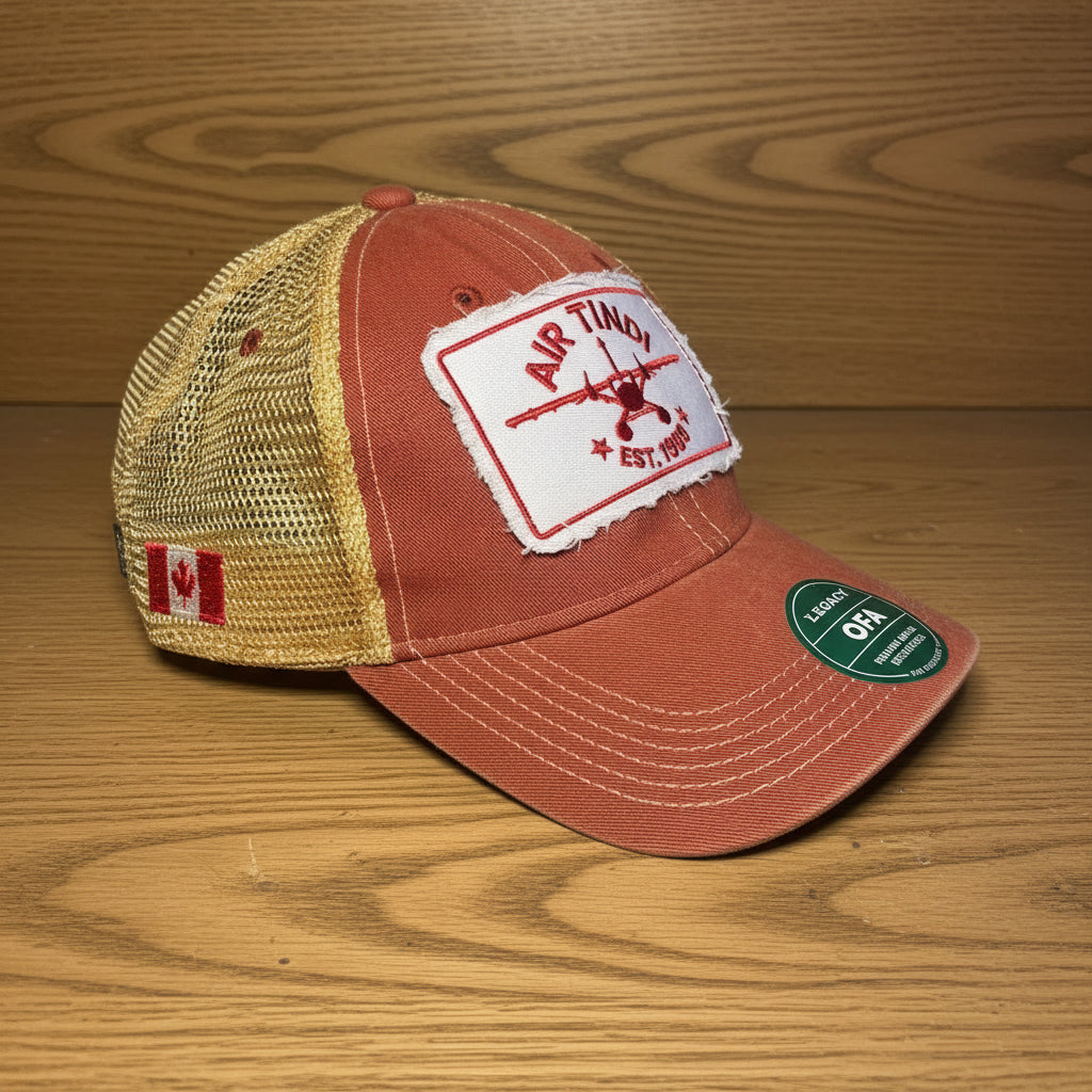 Air Tindi Legacy Trucker Hat in red and gold on a wooden tabletop background