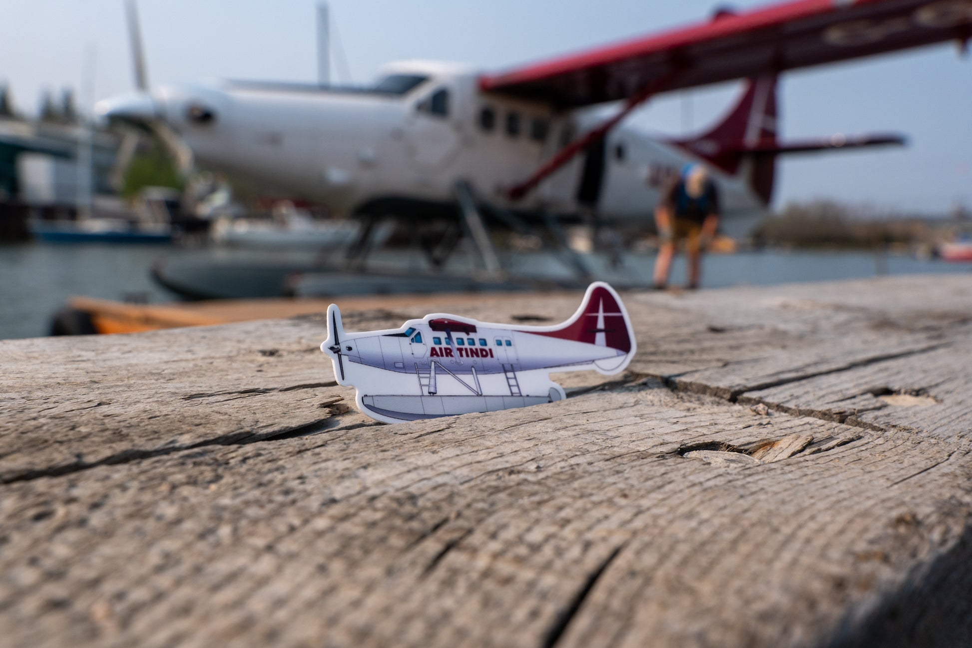 Air Tindi DHC-3T Turbo Otter die-cut sticker on a wooden block with a floatplane in the background