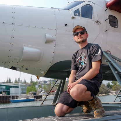 Model wearing an Air Tindi Twin Otter Aurora T-Shirt in mens by a floatplane