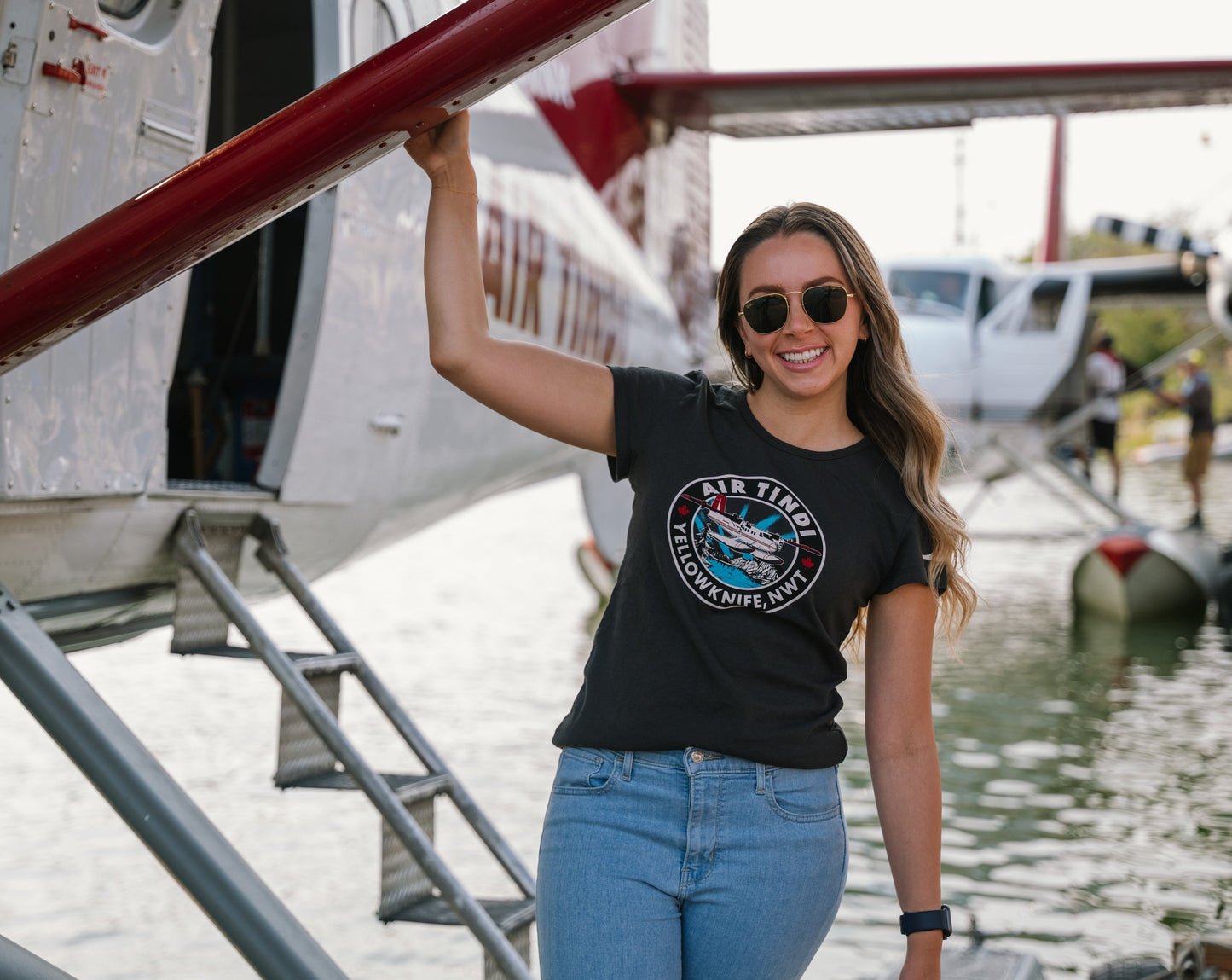 Model wearing an Air Tindi Twin Otter Aurora T-Shirt in ladies by a floatplane