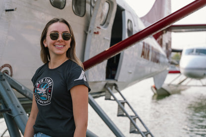 Model wearing an Air Tindi Twin Otter Aurora T-Shirt in ladies by a floatplane