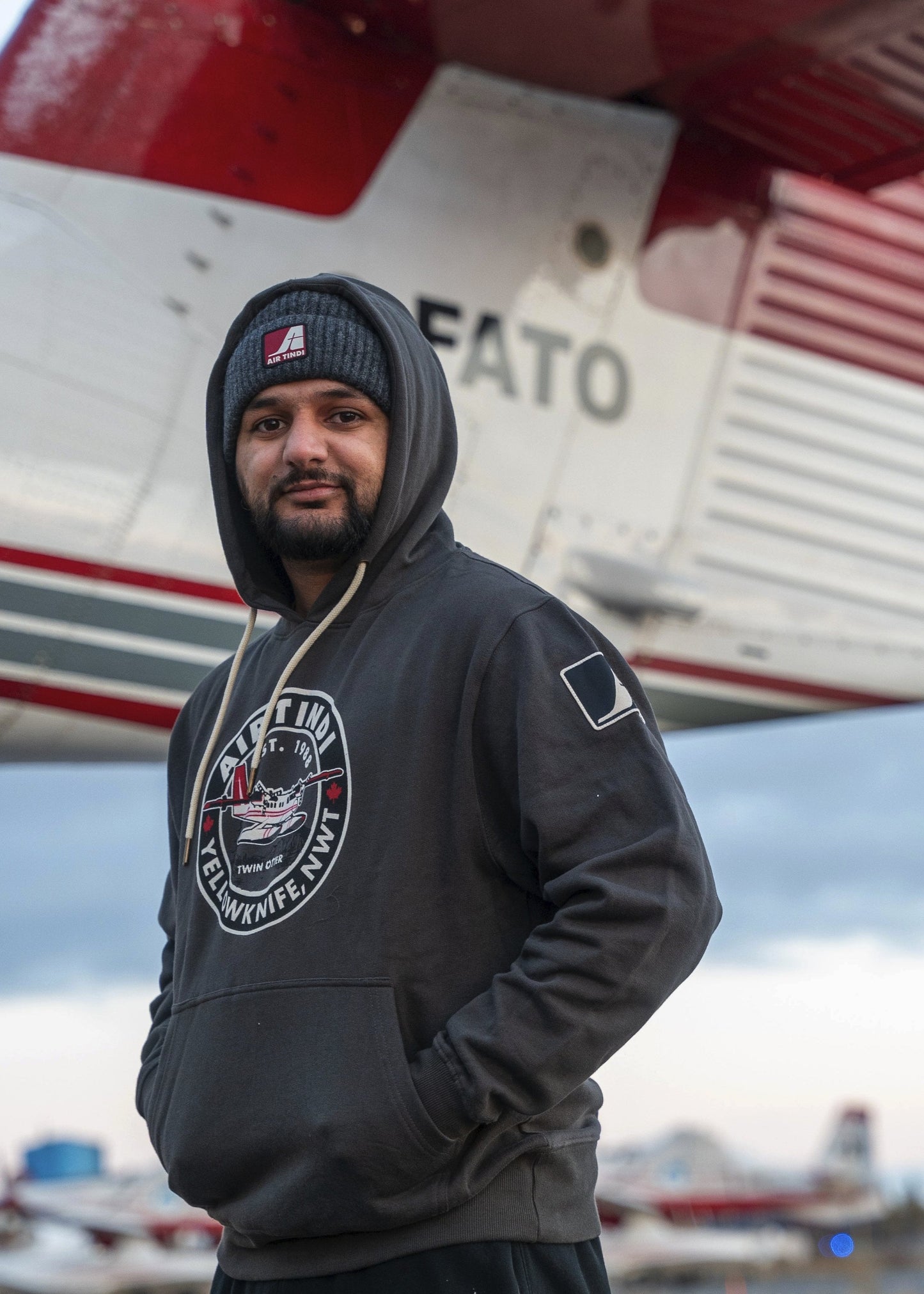 Model wearing an Air Tindi Twin Otter Unisex Hoodie in front of a plane