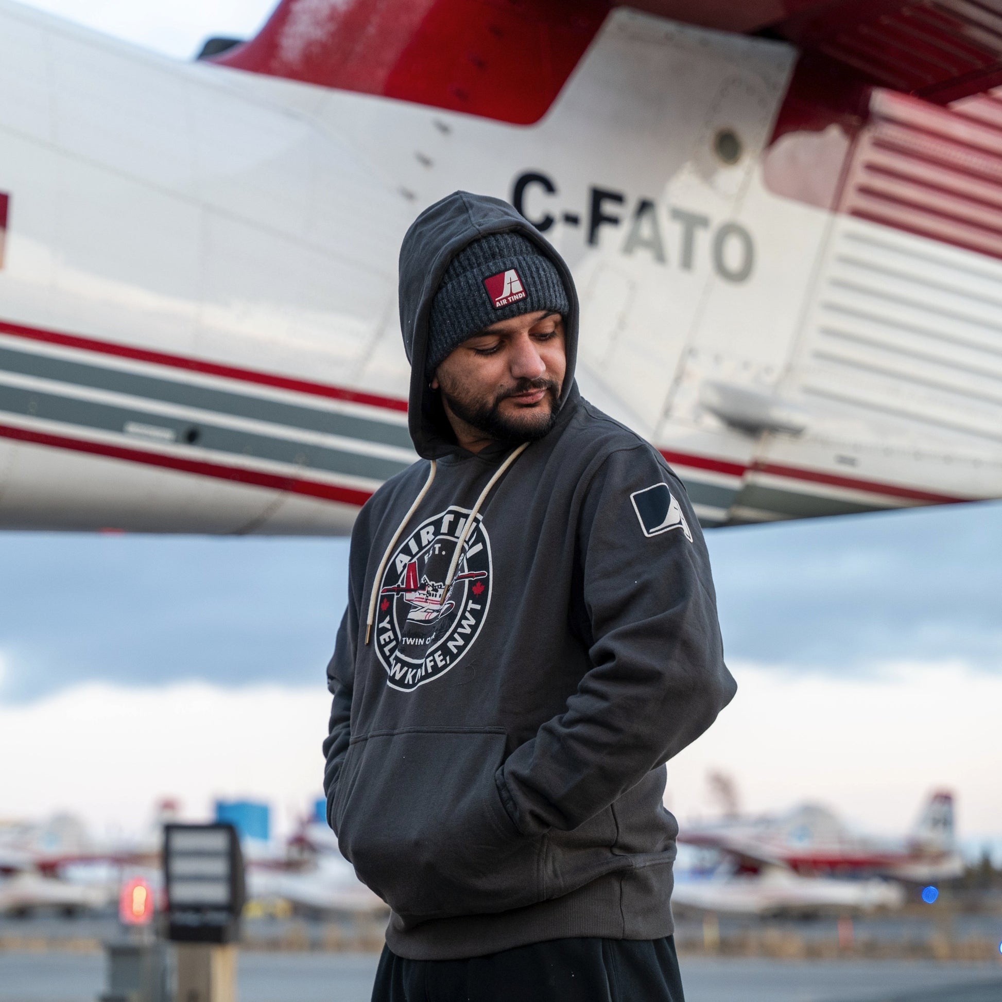 Model wearing an Air Tindi Twin Otter Hoodie in front of a plane